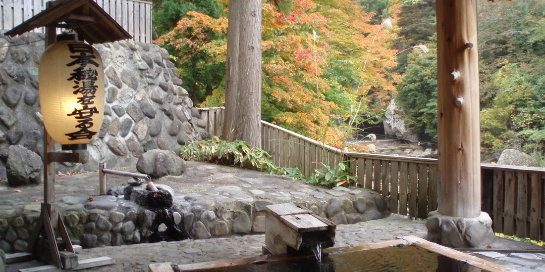 Un bain thermal en plein air en pierre, entouré d’arbres aux couleurs d’automne