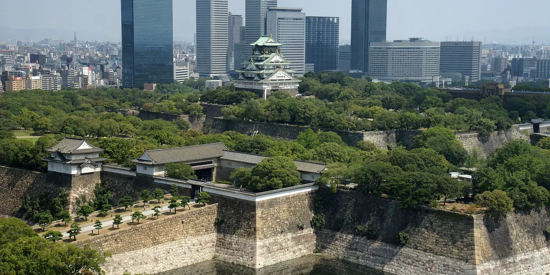 Le château d’Osaka au milieu de ses douves et des arbres, devant les gratte-ciel de la ville