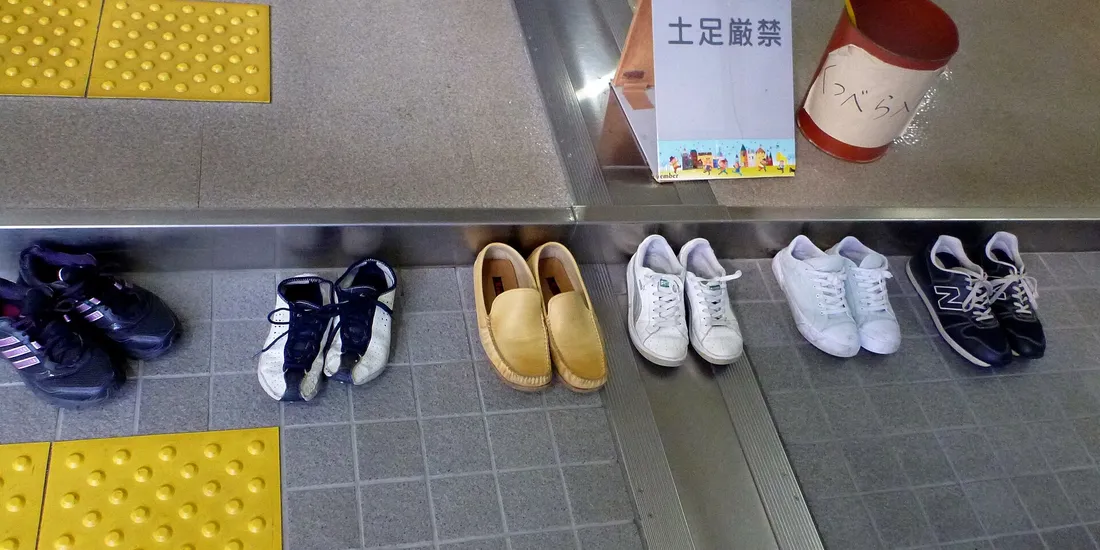 Des chaussures alignées à l’entrée d’un bâtiment japonais, sous un panneau demandant de les retirer
